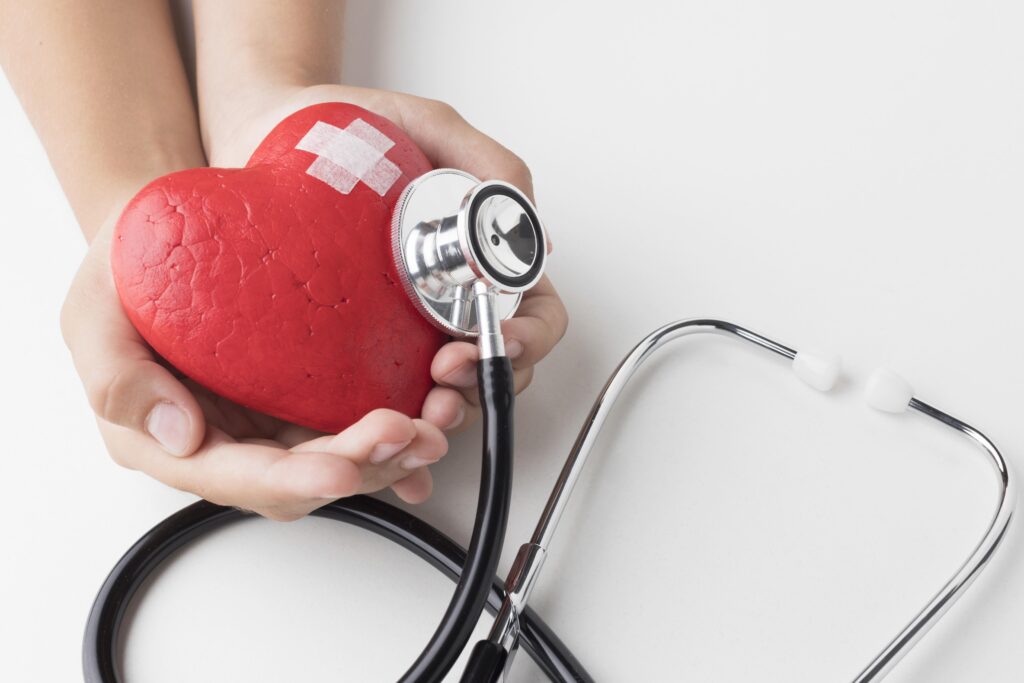The image shows a pair of hands holding a red, heart-shaped object with a bandage on it, along with a stethoscope. This symbolizes heart health and medical care related to the heart.
